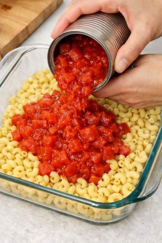Layer raw elbow macaroni with canned diced tomatoes and two basic ingredients in a glass casserole dish for a cozy, crowd-pleasing dinner.